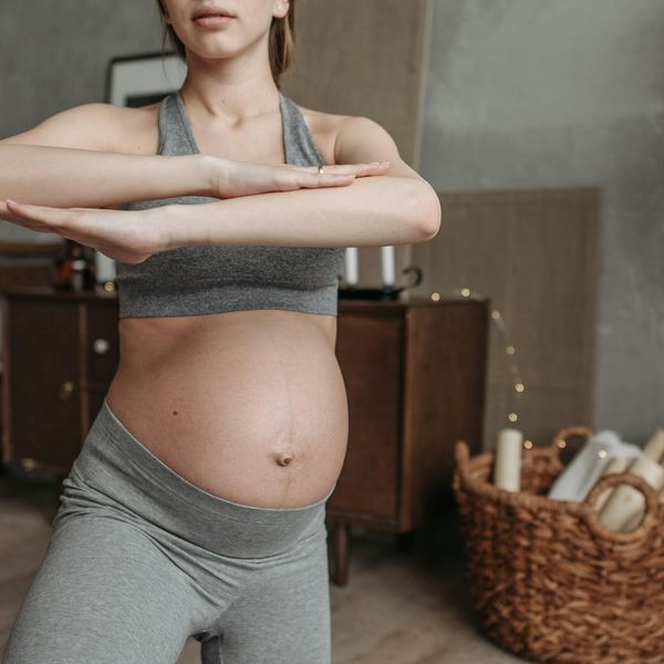 Yoga instructor gently assisting a pregnant woman in a pose.